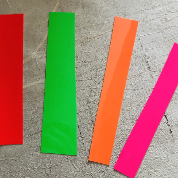 Foto der vier Neonfarben Rot, Grün, Orange und Pink, jeweils als Streifen auf grauem Hintergrund