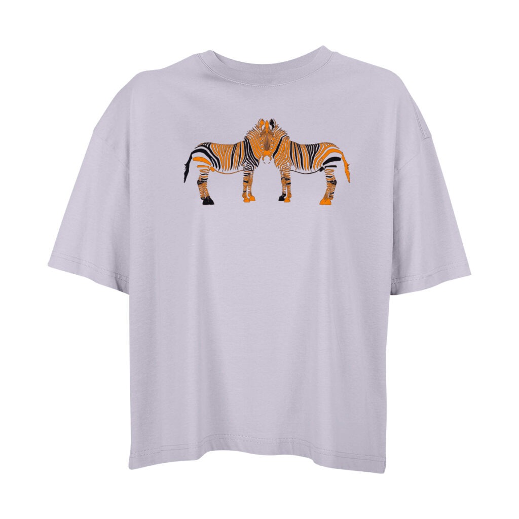 Ein Oversize-Shirt in Flieder, darauf zwei stilisierte Zebras, bestehend aus orangefarbenen und schwarzen Streifen. Von der Seite gezeichnet, sodass zwei Körper sichtbar sind, die aber in einem Kopf verschmelzen.